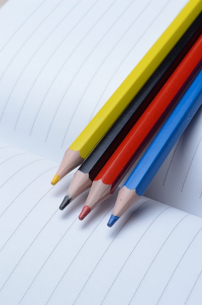 Quatre crayons multicolores - bleu, rouge, jaune, noir. allonger sur un cahier ouvert.