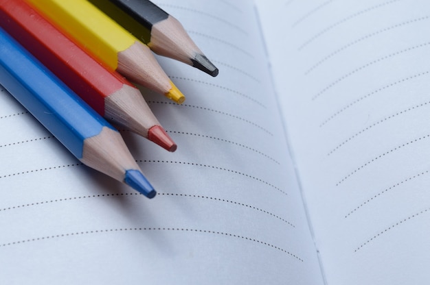 Quatre crayons multicolores - bleu, rouge, jaune, noir. mentir sur un cahier ouvert.