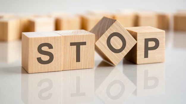 Quatre cubes en bois avec les lettres Stop sur la surface lumineuse d'une table grise. l'inscription sur les cubes se reflète sur la surface de la table. concept d'entreprise.