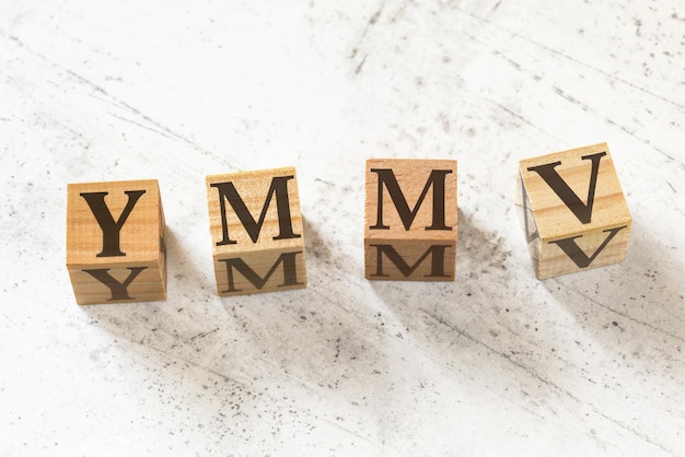 Quatre cubes en bois avec des lettres YMMV signifiant que votre kilométrage peut varier sur une planche de travail blanche.