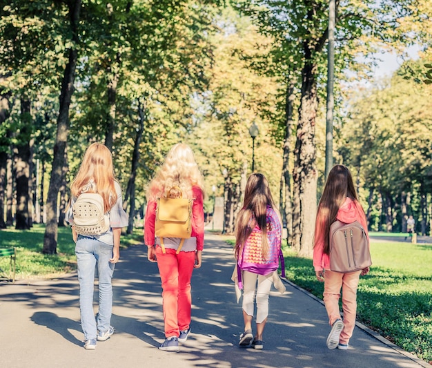 Quatre écolières avec des cartables marchant dans le parc vue arrière