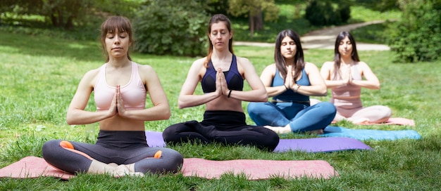 Quatre femmes faisant de la méditation à l'extérieur. Exercices de yoga en groupe dans le parc.