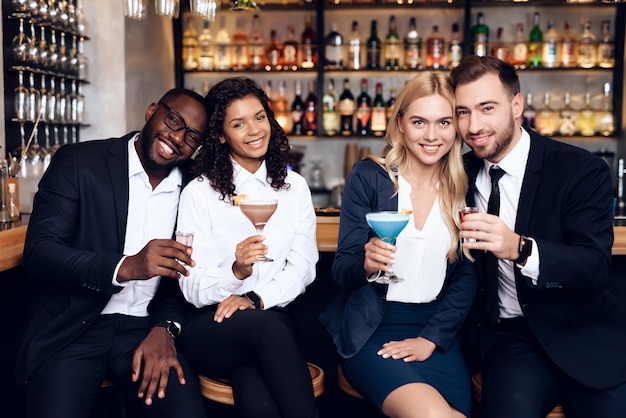 Quatre gars et filles boivent des cocktails dans un bar.