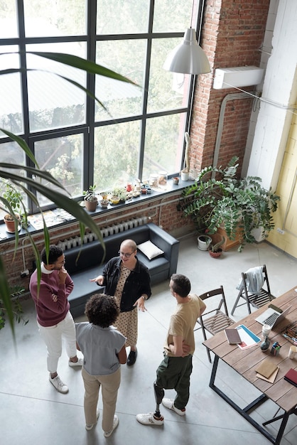 Quatre jeunes employés de bureau contemporains debout près de la table pendant la discussion