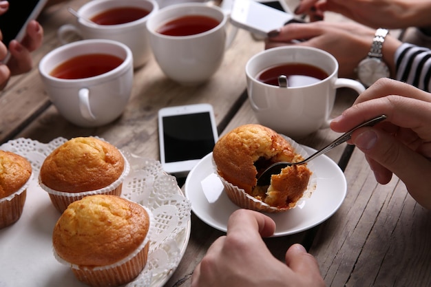 Quatre mains avec des téléphones intelligents tenant des tasses avec du thé sur fond de table en bois