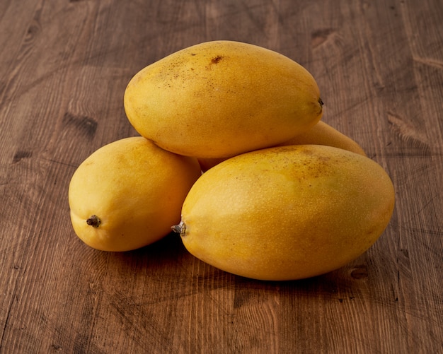 Quatre mangues aux fruits entiers sur table en bois. Gros fruits jaunes mûrs lumineux juteux sur fond sombre