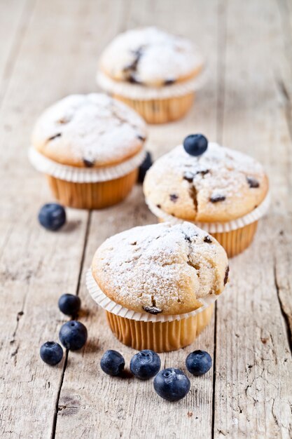 Quatre muffins faits maison frais aux bleuets sur une table en bois rustique.