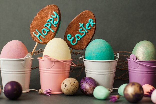 Quatre oeufs de Pâques peints dans des seaux de couleur avec deux cake-pops sur la surface grise libre.