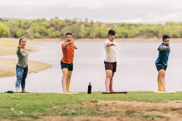 Quatre personnes en ligne levant les bras tout en faisant une pose de yoga à côté d'un lac dans un parc public