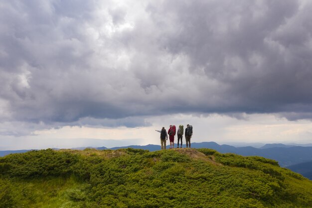 Les quatre personnes avec des sacs à dos debout sur une montagne contre de beaux nuages