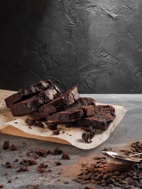 Un quatre-quarts au chocolat en tranches se dresse sur une table grise avec des pépites de chocolat et du cacao.