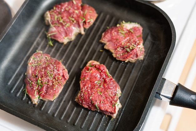 Quatre steaks crus sont frits sur une poêle grillée