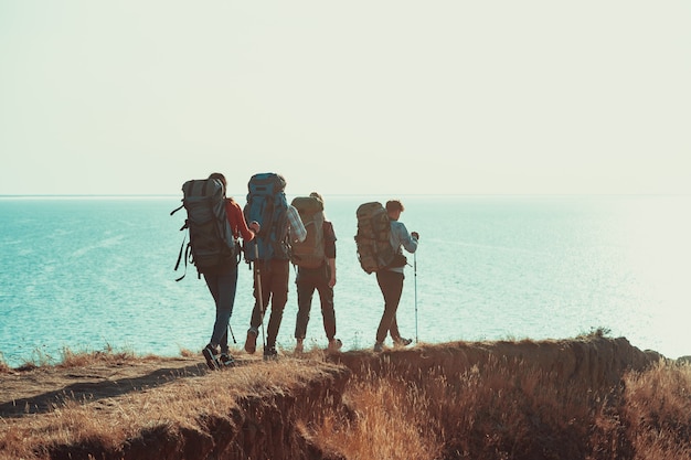 Les quatre touristes avec des sacs à dos marchant le long du rivage de mer