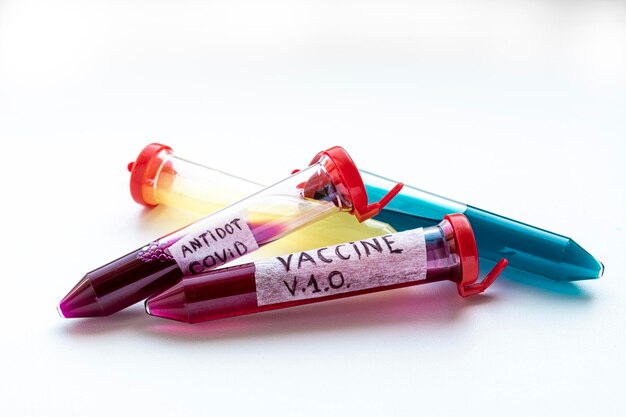 Quatre tubes à essai avec un liquide rouge, jaune et bleu sur fond blanc. Sur l'un des tubes à essai se trouve l'inscription VACCINE. La substance dans les tubes à essai est similaire à un vaccin contre le virus COVID-19