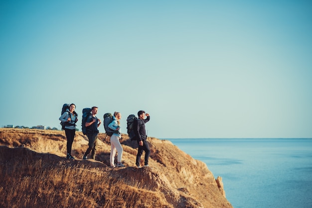 Les quatre voyageurs avec des sacs à dos debout au sommet de la montagne au-dessus de la mer