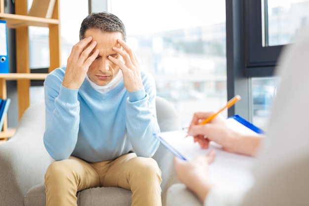 Que faire. Triste homme sans joie déprimé assis en face de son médecin et trouant la tête sans savoir quoi faire