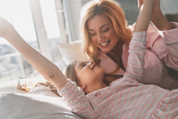 Quel bon sommeil ! Jeune belle mère avec sa mignonne petite fille souriante en position allongée sur le lit à la maison