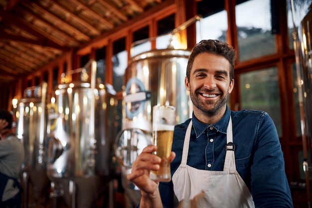 Quel bonheur total Portrait d'un jeune propriétaire d'entreprise joyeux tenant un verre de bière qu'il vient de verser à l'intérieur d'une brasserie de bière pendant la journée