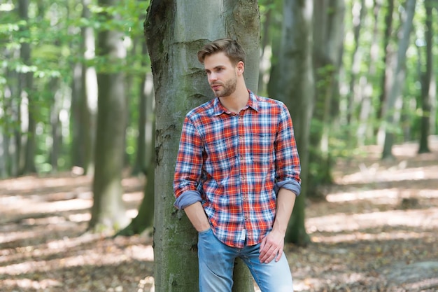 Quelle belle journée homme musclé dans la forêt sexy macho en chemise déboutonnée en plein air homme mal rasé a les cheveux soignés beauté masculine et gars de la mode avec des poils porter une chemise à carreaux style de mode décontracté