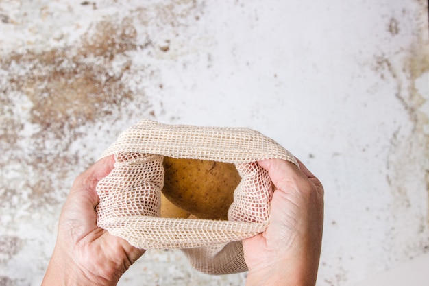 Quelqu'un tenant un sac de légumes en tissu avec une pomme de terre à l'intérieur