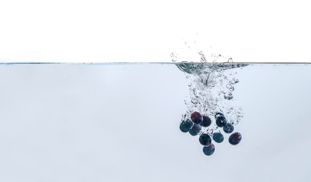 Quelques baies de raisin bleu isolées tombent dans l'eau avec des éclaboussures