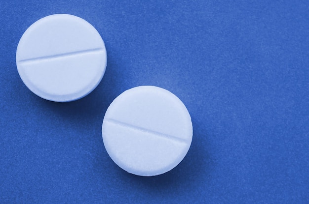 Quelques comprimés blancs reposent sur une surface d'arrière-plan de couleur bleu classique fantôme lumineux Image d'arrière-plan sur des sujets médicaux et pharmaceutiques