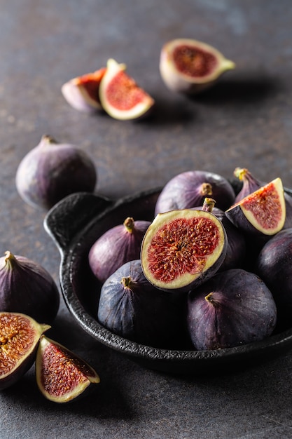 Quelques figues dans un bol noir sur une table en béton foncé.