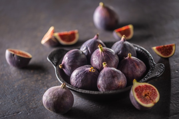 Quelques figues dans un bol noir sur une table en béton foncé.