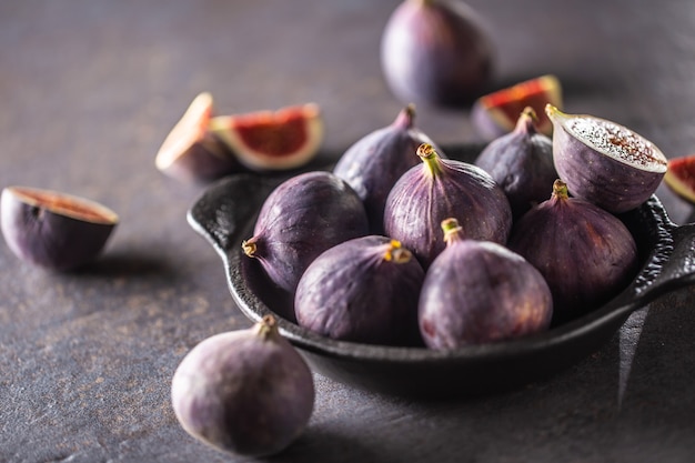 Quelques figues dans un bol noir sur une table en béton foncé.