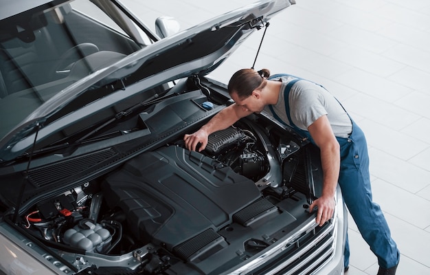 Quelques mouvements de finition. L'homme en uniforme bleu travaille avec une voiture cassée. Faire des réparations.