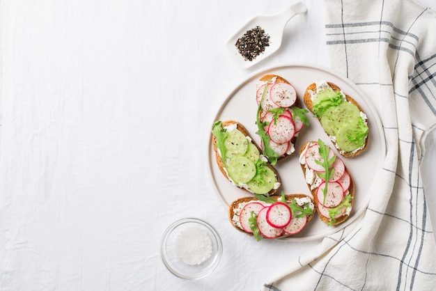 Quelques toasts de radis et de concombre avec de la ricotta et de la salade sur assiette avec du sel et du papier