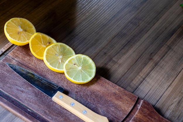 Quelques tranches de citron coupées sur une planche de bois à côté d'un couteau sur un fond rustique.