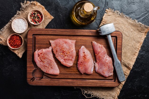 Quelques tranches de viande de dinde crue sur une planche à découper en bois sur fond noir