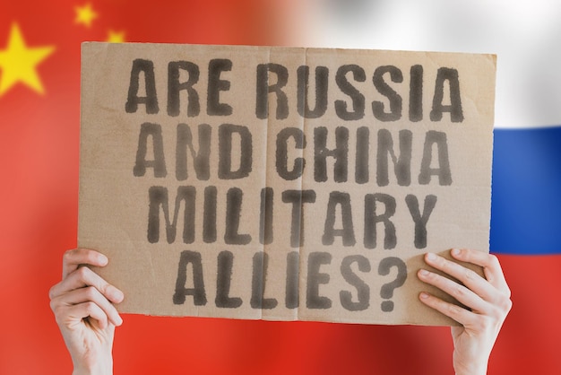 La question « La Russie et la Chine sont-elles des alliés militaires ? » sur une bannière dans la main des hommes avec un drapeau russe et chinois flou en arrière-plan. Soutien. Arme. Pékin