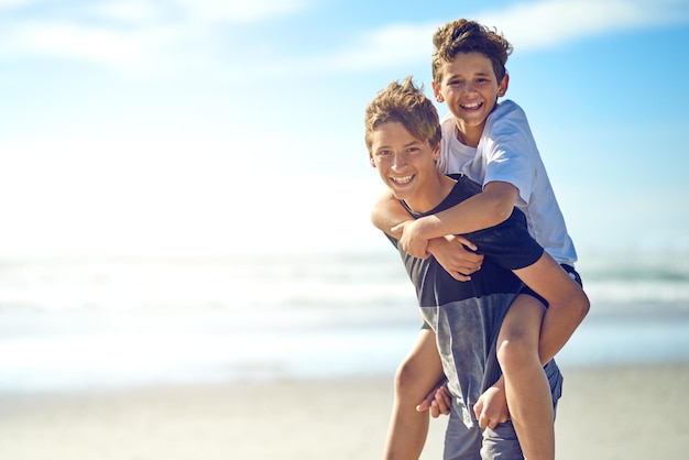 Qui a besoin d'un super-héros quand on a un grand frère Portrait d'un jeune garçon heureux donnant à son petit frère un tour de ferroutage sur la plage