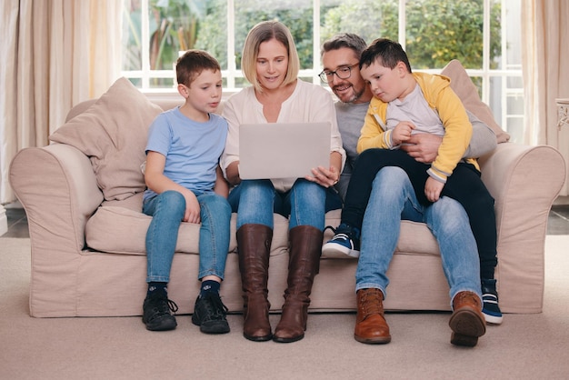 Qui reçoit les collations Photo d'une jeune famille qui se lie tout en utilisant un ordinateur portable sur le canapé ensemble à la maison