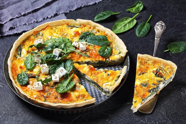 Quiche au fromage cheddar et épinards feta dans un plat allant au four sur une planche en bois sur une table en béton gris, cuisine française