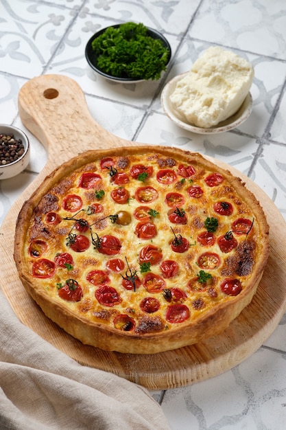 Quiche au poulet, tomates cerises et fromage. Tarte française ouverte appétissante. Plat sur une planche de bois dans la cuisine. Verticalement.