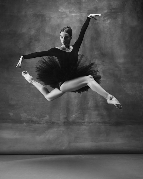 Équilibré. Danse de ballerine classique gracieuse, posant isolé sur fond de studio sombre. Tutu noir élégance. Concept de grâce, de mouvement, d'action et de mouvement. Semble en apesanteur, flexible. À la mode.