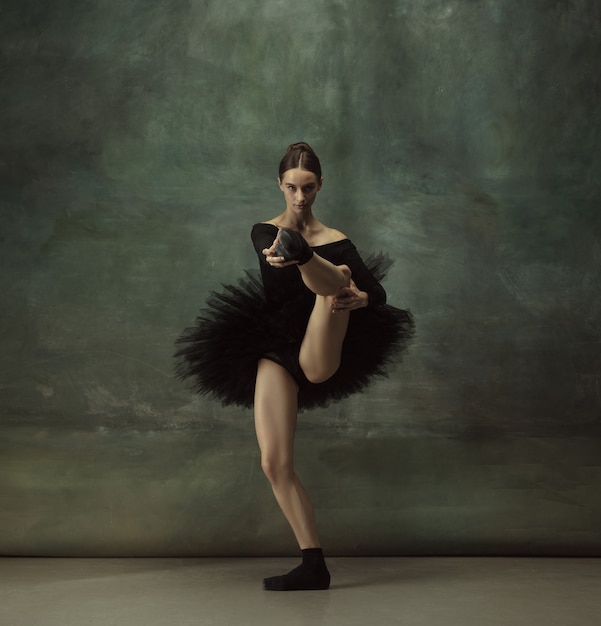 Équilibré. Danse de ballerine classique gracieuse, posant isolée sur le mur sombre du studio