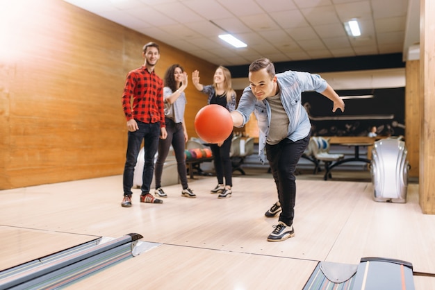 Quilleur mâle lance la balle sur la voie. Équipes de bowling jouant le jeu en club, loisirs actifs