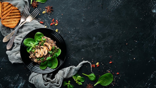 Quinoa aux épinards et champignons Dans une assiette noire sur un fond en bois Vue de dessus Espace libre pour votre texte Mise à plat