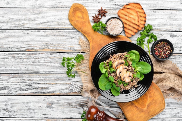 Quinoa aux épinards et champignons Dans une assiette noire sur un fond en bois Vue de dessus Espace libre pour votre texte Mise à plat