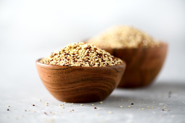 Quinoa organique cru blanc et rouge dans un bol en bois et le romarin sur fond gris. Ingrédients alimentaires sains.