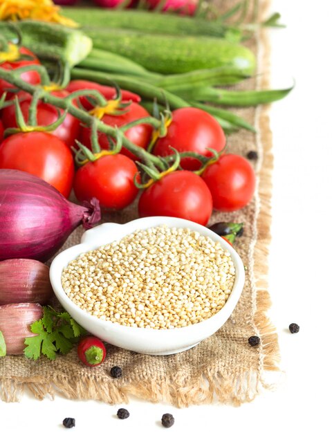 Quinoa sec cru dans un bol et légumes sur une toile de jute isoler sur blanc close up