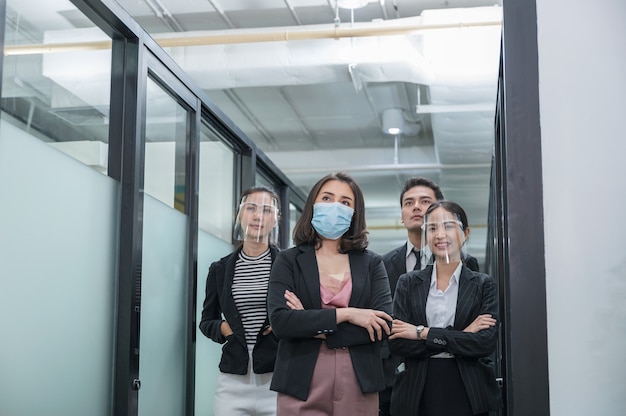 Équipe des affaires asiatiques confiant portant un masque facial et un écran facial au couloir dans un bureau moderne