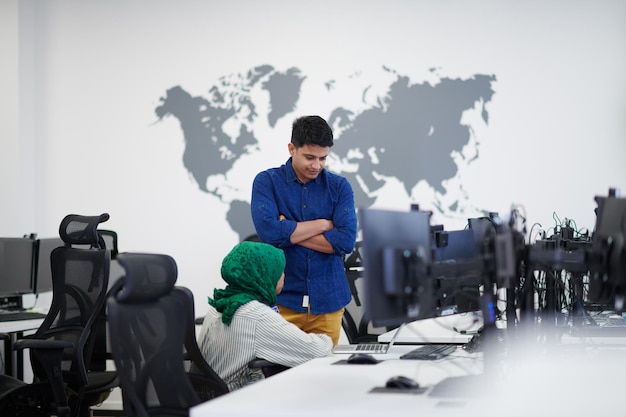 Équipe d'affaires de démarrage multiethnique Femme arabe portant un hijab lors d'une réunion dans un brainstorming intérieur de bureau ouvert moderne, travaillant sur un ordinateur portable et un ordinateur de bureau