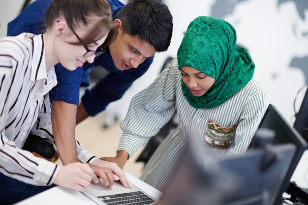 Équipe d'affaires de démarrage multiethnique Femme arabe portant un hijab lors d'une réunion dans un brainstorming intérieur de bureau ouvert moderne, travaillant sur un ordinateur portable et un ordinateur de bureau