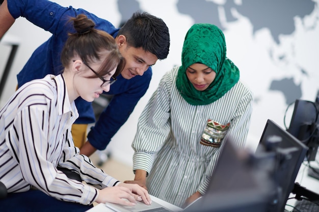 Équipe d'affaires de démarrage multiethnique Femme arabe portant un hijab lors d'une réunion dans un brainstorming intérieur de bureau ouvert moderne, travaillant sur un ordinateur portable et un ordinateur de bureau