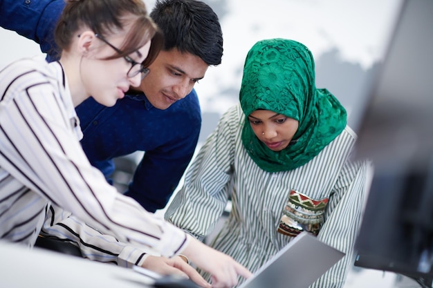 Équipe d'affaires de démarrage multiethnique Femme arabe portant un hijab lors d'une réunion dans un brainstorming intérieur de bureau ouvert moderne, travaillant sur un ordinateur portable et un ordinateur de bureau